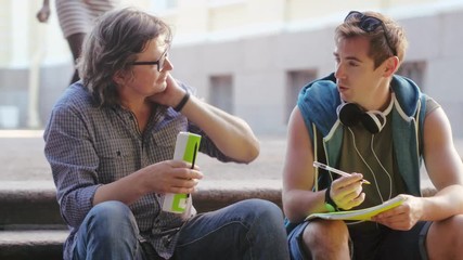 European student and professor sitting on stairs outdoors