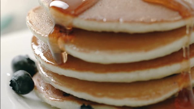 Pancakes with slow pour of maple syrup and blueberries on breakfast plate. 