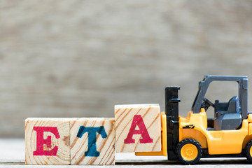 Toy forklift hold letter block A in word ETA (abbreviation of estimated time of arrival) on wood background - obrazy, fototapety, plakaty