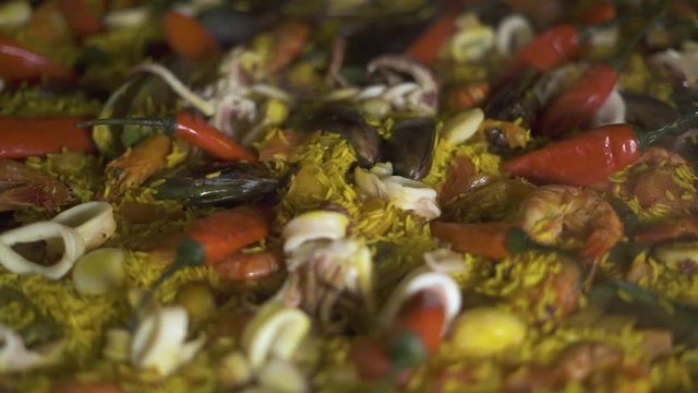 Traditional paella with mussels, shrimps, calamari and hot peppers in pan. Close up. Cooking spanish food paella with red peppers and fresh seafood in pan. Spanish cuisine concept.