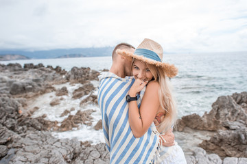 young man hugging beautiful smiling girlfriend on rocky beach in montenegro