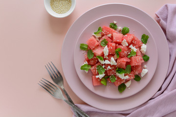 Summer watermelon salad with feta cheese, sesame seeds and mint leaves on pink plate. Healthy eating concept
