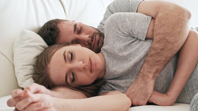 Handheld PAN of bearded man with closed eyes lying in bed and hugging beautiful girlfriend holding his hand