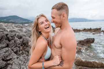 side view of happy young couple hugging and laughing on rocky beach in montenegro