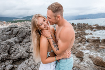 happy young couple hugging and laughing on rocky beach in montenegro