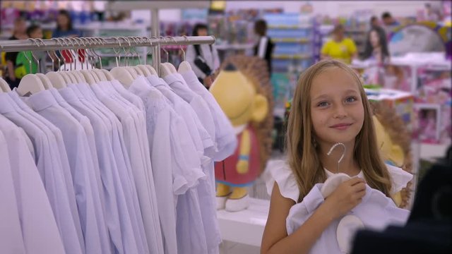 Adorable smiling girl trying and fitting white blouse in boutique