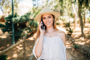 Young beautiful woman in straw hat in city park speaks by mobile phone outdoors. Summer mood.