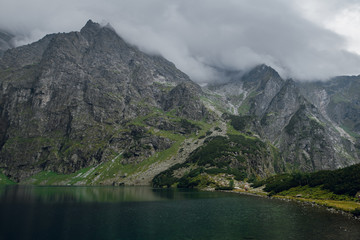 Beautiful view of foggy mountains cover by dark clouds and green forest with a reflection in a lake. Morskie Oko. Marine Eye. High Tatras, Zakopane, Poland