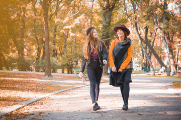 Obraz premium Two teenage girls are having fun in the park, autumn outfit. Funny girl friends throwing dry leaves in the city in autumn. Happy family on autumn walk!