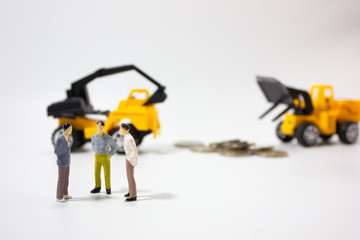 three miniature businessman with construction car and coins background.