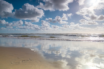 Bank of the blue sea with wet sand and clouds