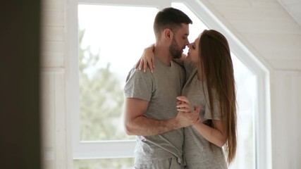 Handheld shot of happy young couple hugging and kissing by panoramic window in bedroom