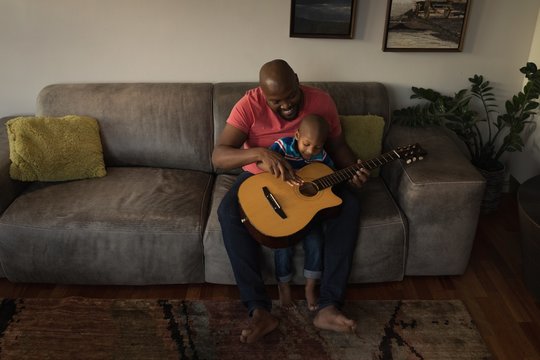Father and son playing with guitar in living room