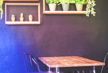 Wooden table with metal chairs placed close to the wall in coffee shop, on the wall has cute decoration of artificial plants and cactus candles, photo is in blue and purple tone