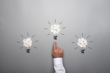 Three light bulbs formed by scattered white puzzle pieces with hand of a businessman