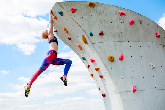 Photo of sporty girl in leggings hanging on wall for rock climbing against blue sky