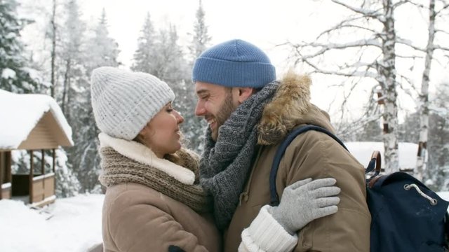 Young affectionate couple kissing, hugging and smiling while spending winter day outdoors in the park