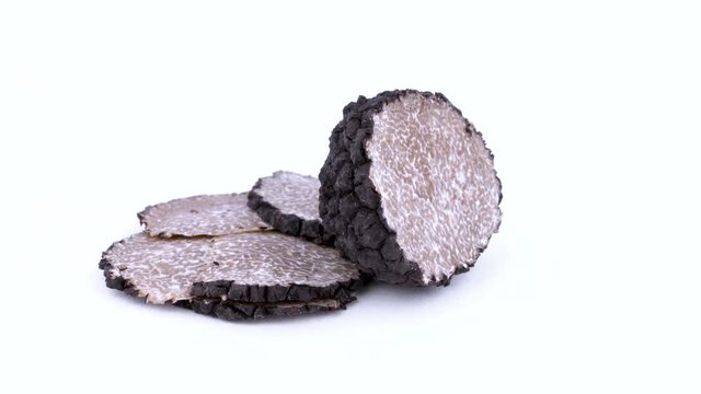 Heap of black truffle slices and one half of the truffle mushroom. Rotating on the on the turn table. Isolated on the white background. Closeup.