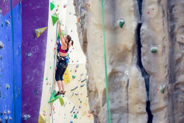 Photo of young girl with safety rope practicing on climbing wall in gym.
