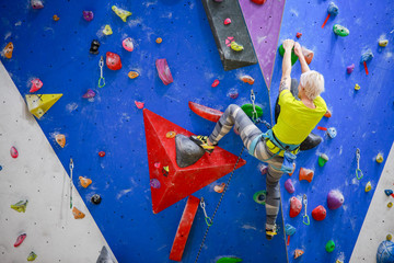 Photo from back of sports blonde climbing blue wall into gym