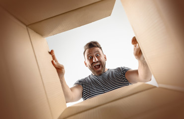 The surprised man unpacking, opening carton box and looking inside. The package, delivery,...