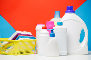 Photo of different bottles of cleaning products and colored towels in basket isolated on red, blue background