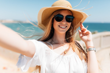 Fototapeta premium Portrait of happy adorable woman making selfie or photo of herself, stands against sea background. People and leisure concept
