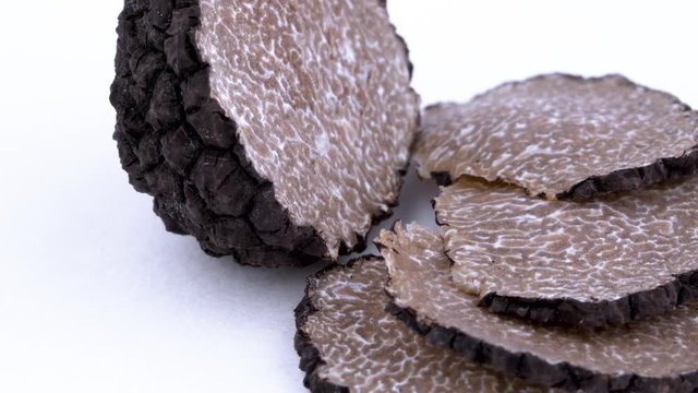 Macro of black truffle slices and one-half of the truffle mushroom slowly rotating on the on the turntable. Isolated on the white background. Closeup.