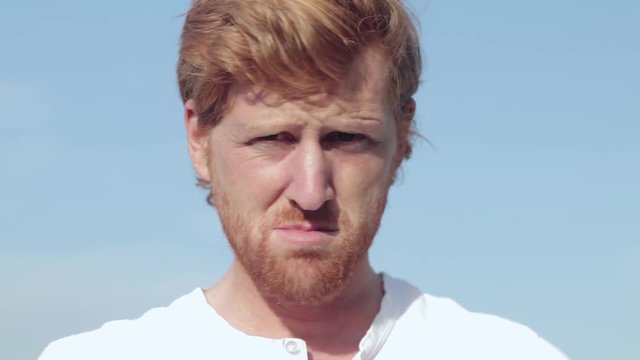 A close shot of the face of a ginger haired man shaking his head and frowning in disappointment.