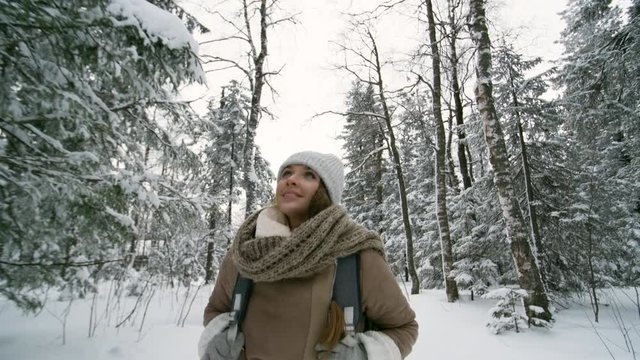 Happy beautiful woman looking around and smiling while walking in forest at snowy winter day
