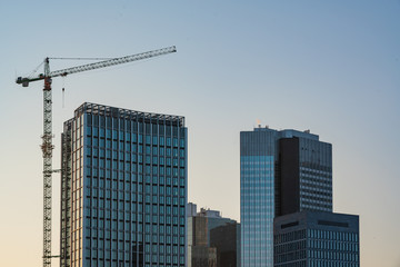 Fototapeta na wymiar lifting crane, tower crane and modern building under development construction. Construction of a modern high-rise business center in morning sunlight - Germany