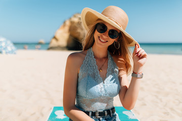 Young attractive woman wearing stylish straw and sunglasses hat sitting and relaxing under the sun...