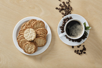 Cup of black coffee whit cookies on white plate and wooden background. Top view.