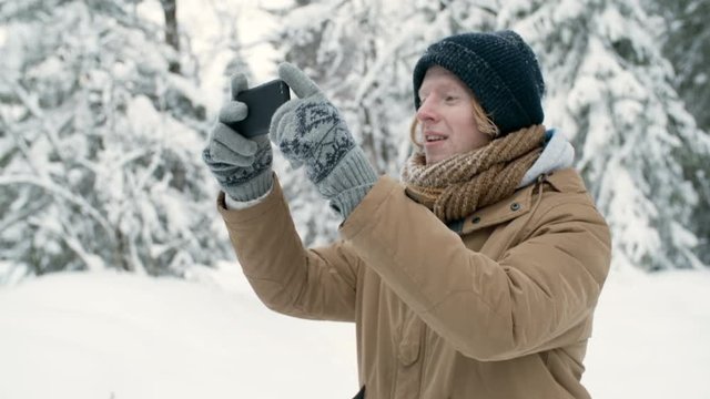 Young man taking picture of winter nature with smartphone while hiking in national park