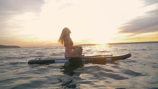 One woman floats on waves, meditating, side view. Surfing woman sits on her board in a pose, resting.