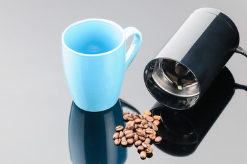 Fototapeta na wymiar Coffee grinder with coffe beans and mug on the grey mirror background. Copy space.