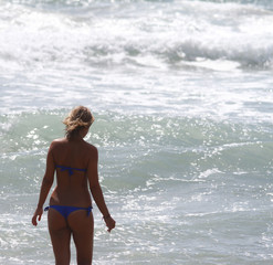 Fototapeta na wymiar Beautiful girl, seen from behind, with bikini, who enters the water. Rough sea in the background