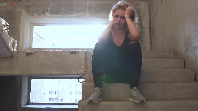 Young unhappy girl is sitting at the stairs in an abandoned building