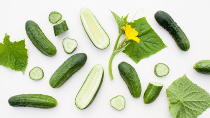 Young cucumbers with cut cucumber and leaf on white