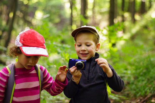 Portrait of children taking photos with a camera in the forest. Scene in the summer, large blur background.