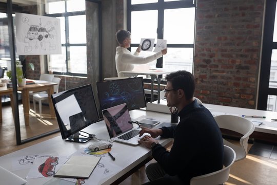 Businessman using laptop while his colleagues looking at sketch