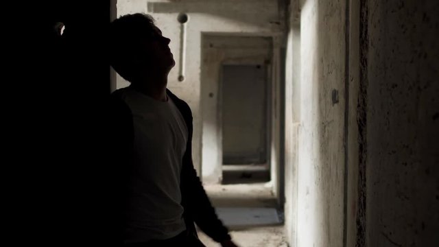 Yound bad looking man leans against the walls in an abandoned building