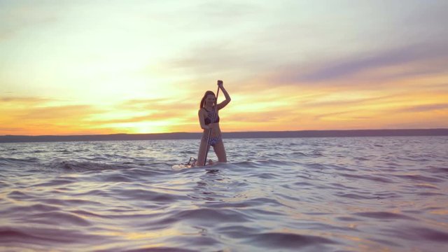 Happy woman floats on a surfboard. Professional surfer rides a board in the evening.