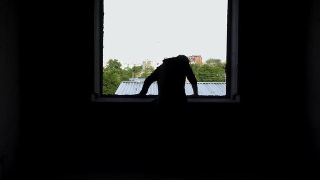 Yound bad looking man looks out the window of an abandoned house