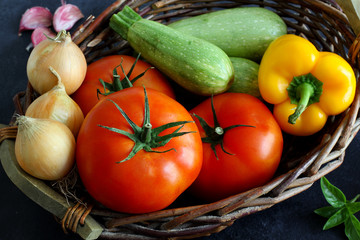 Variety of fresh vegetables in market basket on dark background, high angle view