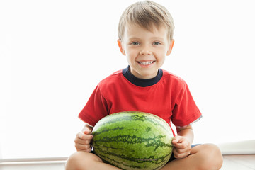 Fototapeta premium A cute boy and a big green watermelon. The child smiles and rejoices.