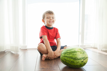 Fototapeta premium A cute boy and a big green watermelon. The child smiles and rejoices.