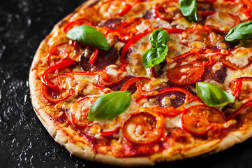 Pizza with Mozzarella cheese, Ham, Tomatoes, salami, pepper, pepperoni Spices and Fresh Basil. Italian pizza.on black background
