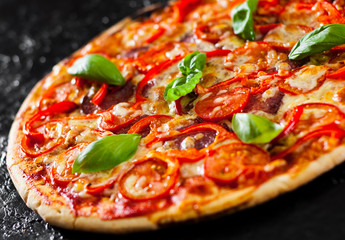 Pizza with Mozzarella cheese, Ham, Tomatoes, salami, pepper, pepperoni Spices and Fresh Basil. Italian pizza.on black background