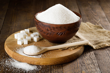 Bowl and spoon full of sugar on wooden background
